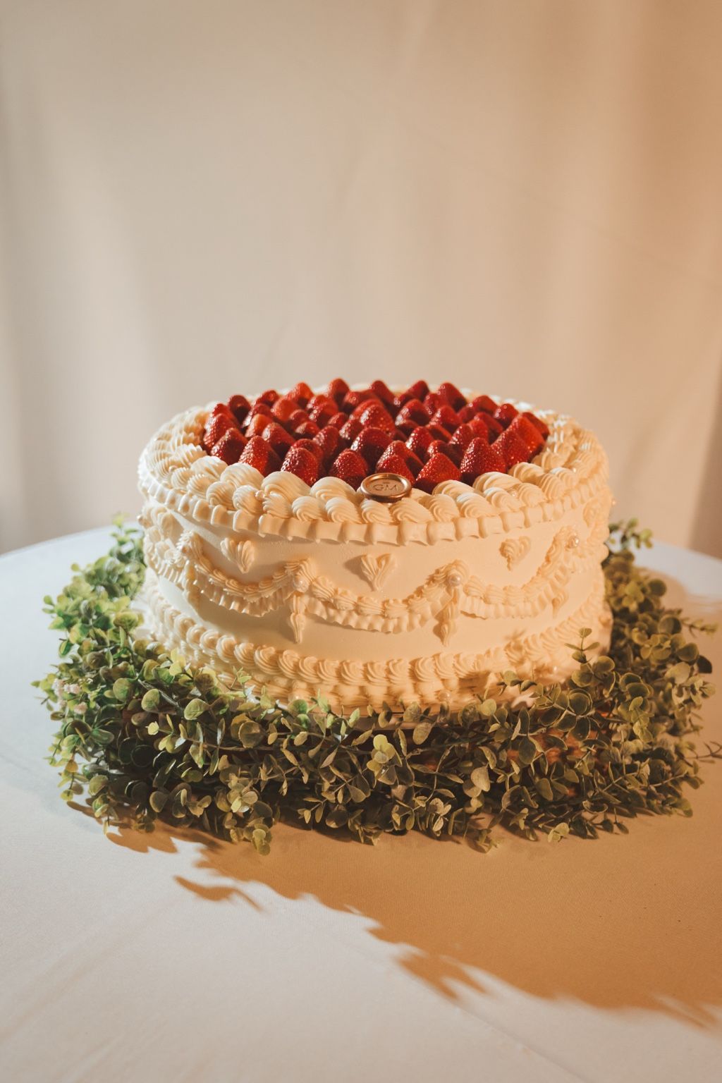 A buttercream cake topped with strawberries, set on a ring of greenery