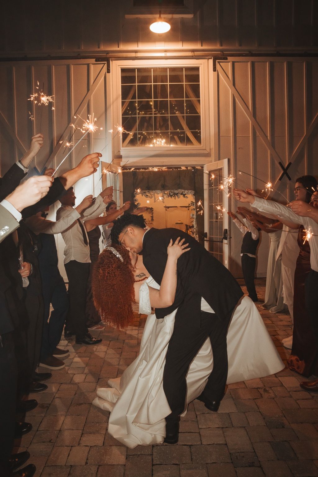A couple kissing beneath a sparkler send-off lined with guests