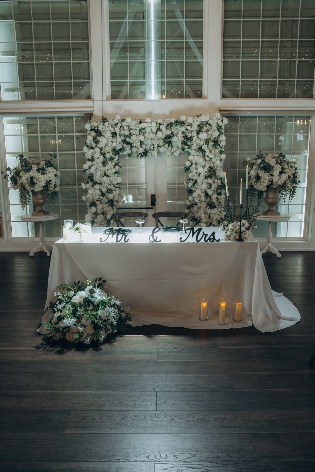 A sweetheart table framed by a white floral arch and candlelight